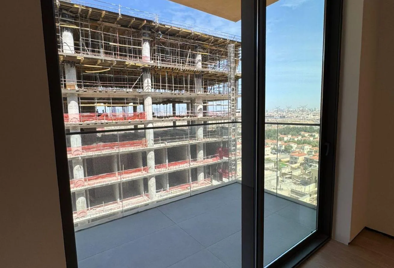 Photo of the balcony through a glass door, facing a building under construction
