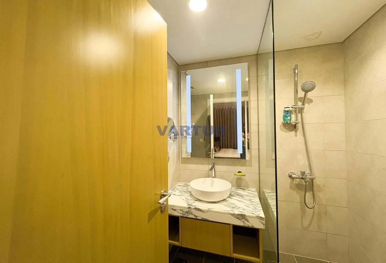 Photo of the bathroom, with a marble vanity, a lit mirror and a glass shower