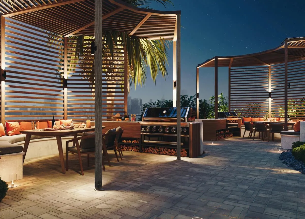An outdoor dining table under a slatted timber pergola at dusk, a grill counter along the far wall