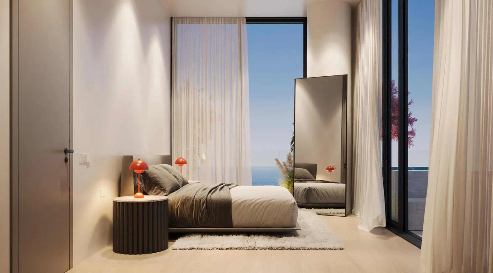 A bedroom with an armchair by the window and the sea beyond the glazing