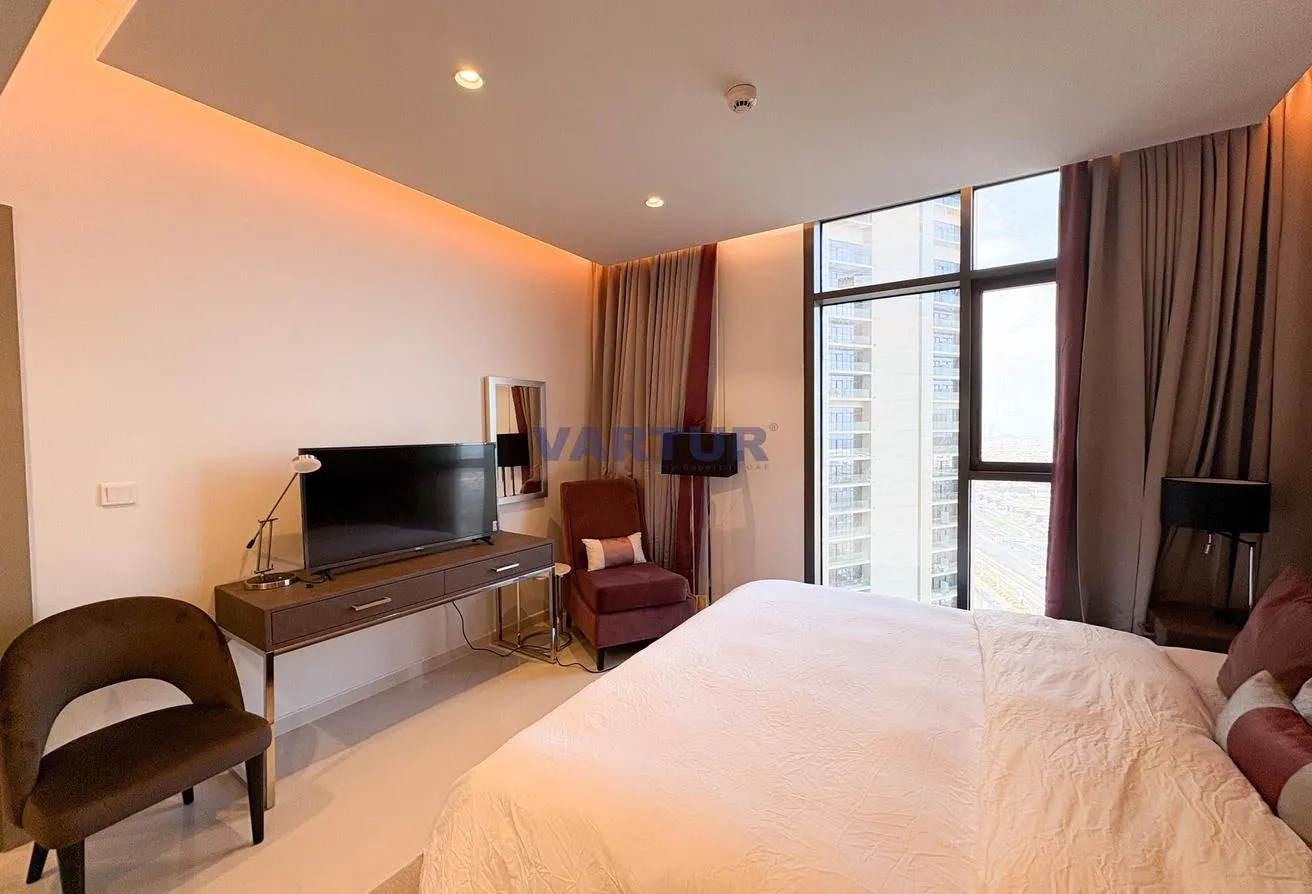 Photo of the bedroom looking towards the window, with a desk, a TV and an armchair