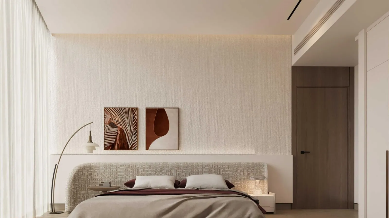 A bedroom in a cream palette, two small framed prints above the bed and a slim floor lamp beside it