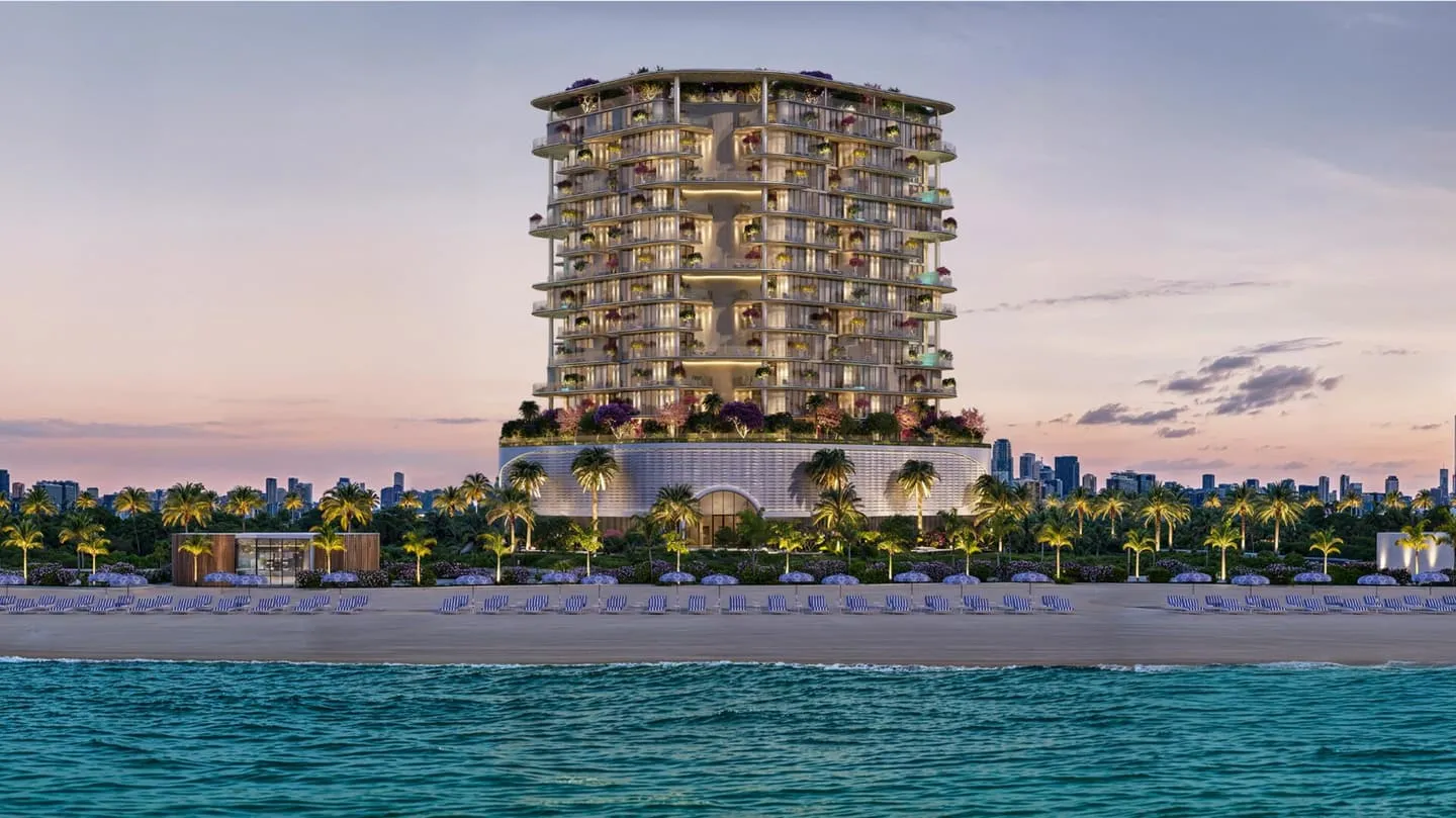 The building seen across turquoise water, standing low on the shoreline with the Dubai skyline faint behind it