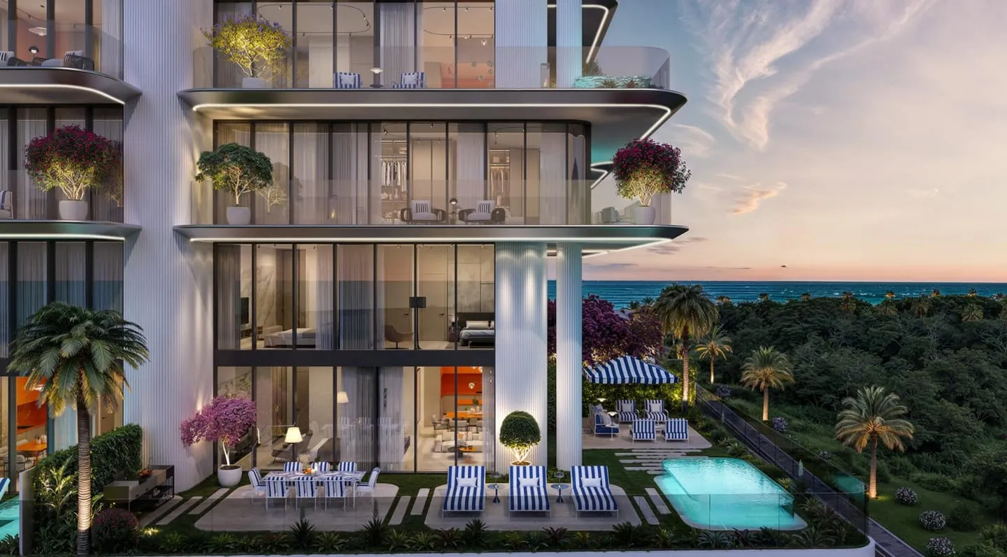 The facade at twilight above the lit swimming pool, palms and flowering trees framing the terraces