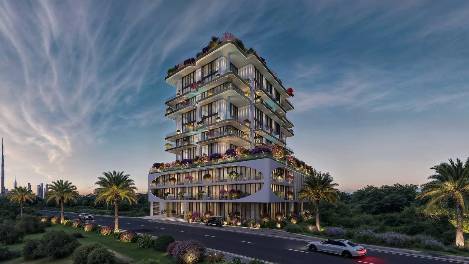 The whole building seen from across the road at dusk, palms along the kerb under a clear evening sky