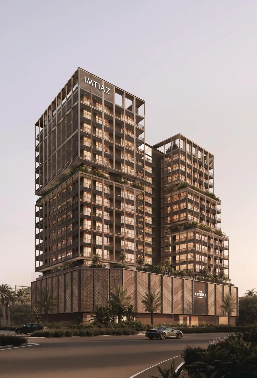 The building at dusk from the corner, offset volumes in a bronze frame with the developer's name on the roof and the project's name on the podium
