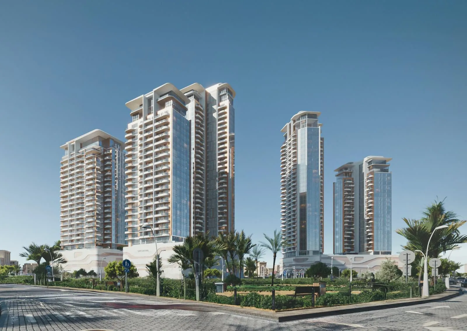 The towers from street level in daylight, pale facades stepping back above palms and a low garden wall
