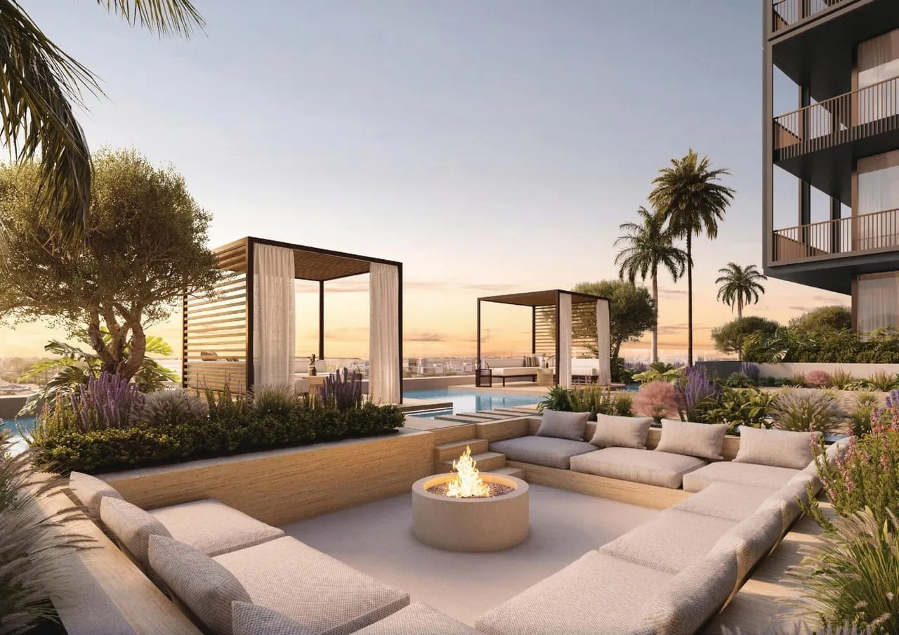 A sunken seating terrace at sunset, a fire bowl at its centre and curtained cabanas beside the pool