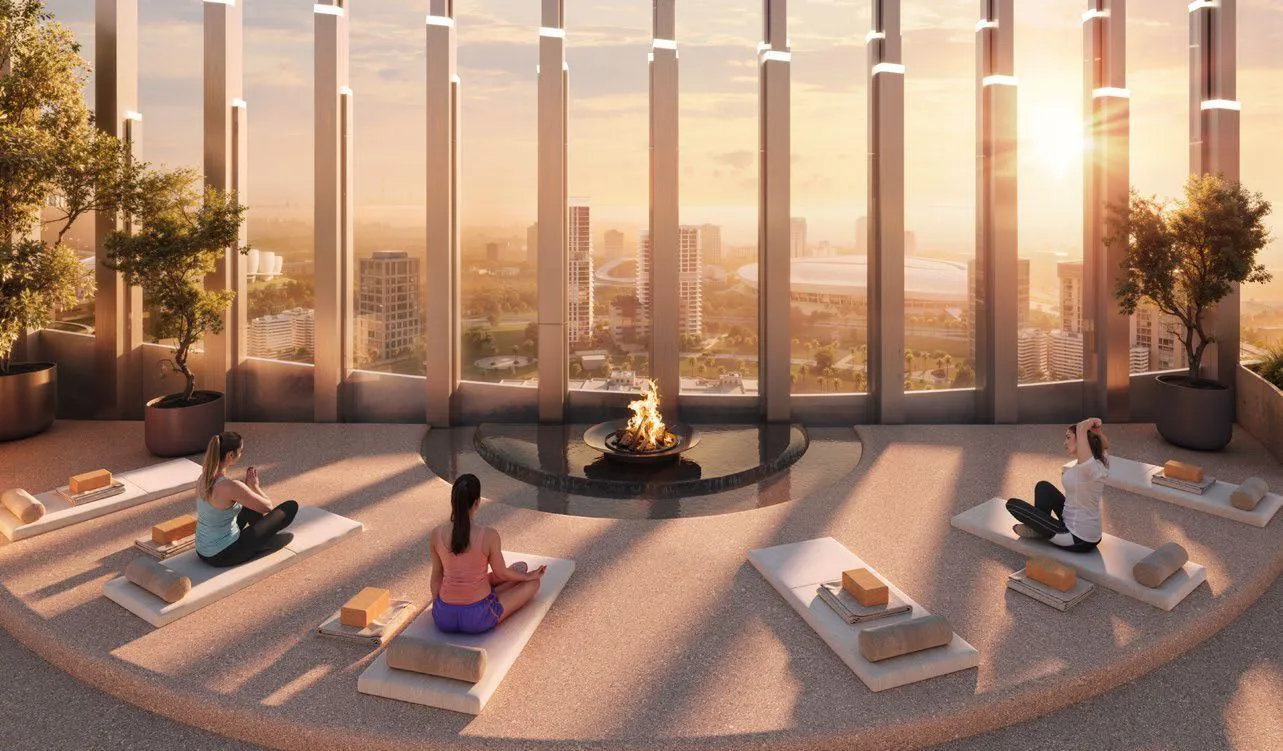 A curved glazed lounge at sunset, people on mats and loungers along full height windows with planting between them