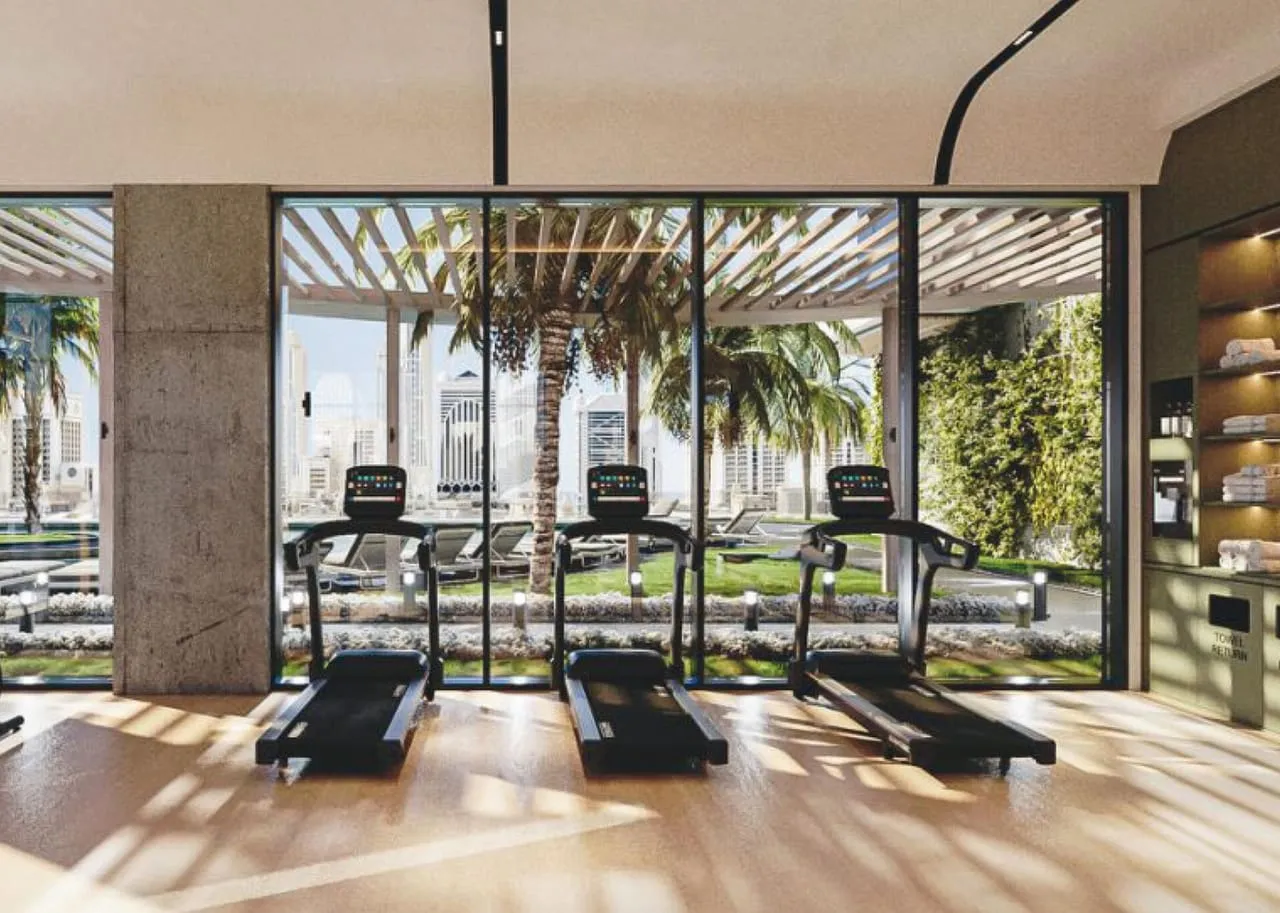 The gym, a row of treadmills facing full height glass with palms outside