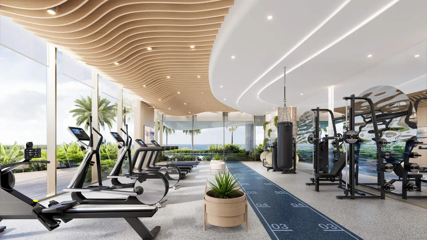 The gym, treadmills and weight machines in a row along the glass with planting at the far end