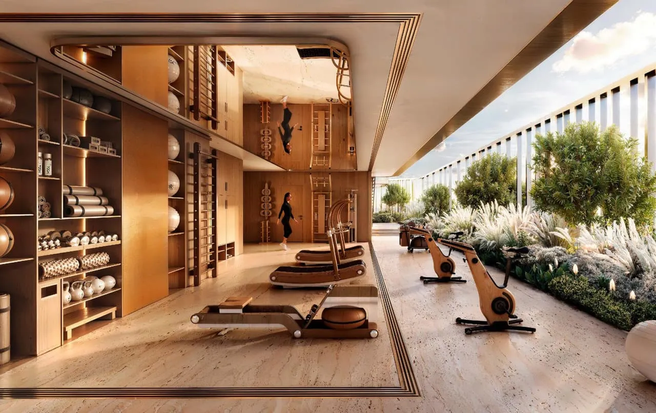 A gym along the terrace edge, rowing machines and benches on travertine with planting outside the glass