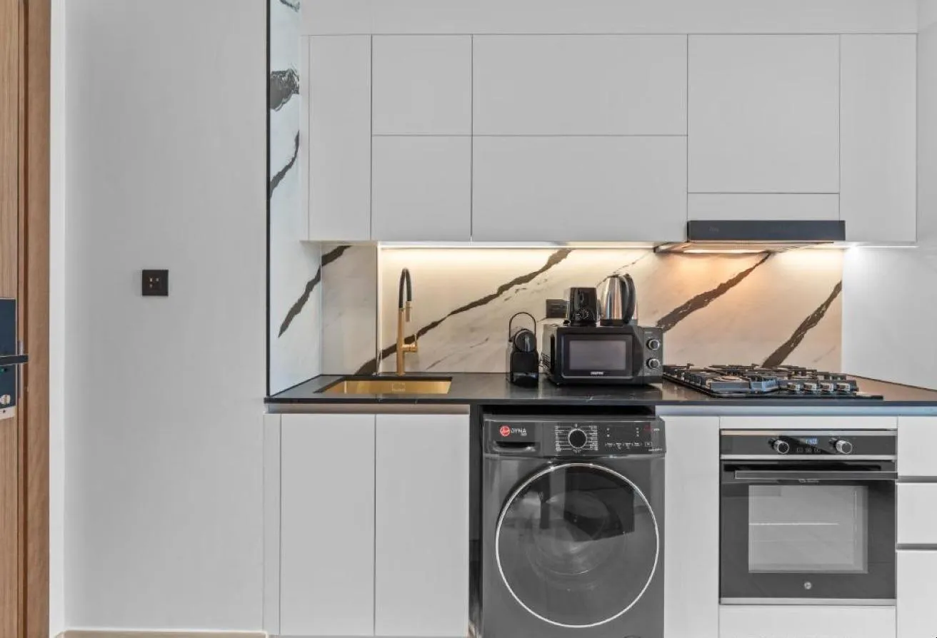 Photo of the kitchen, with white cabinets, a washing machine and a built-in oven