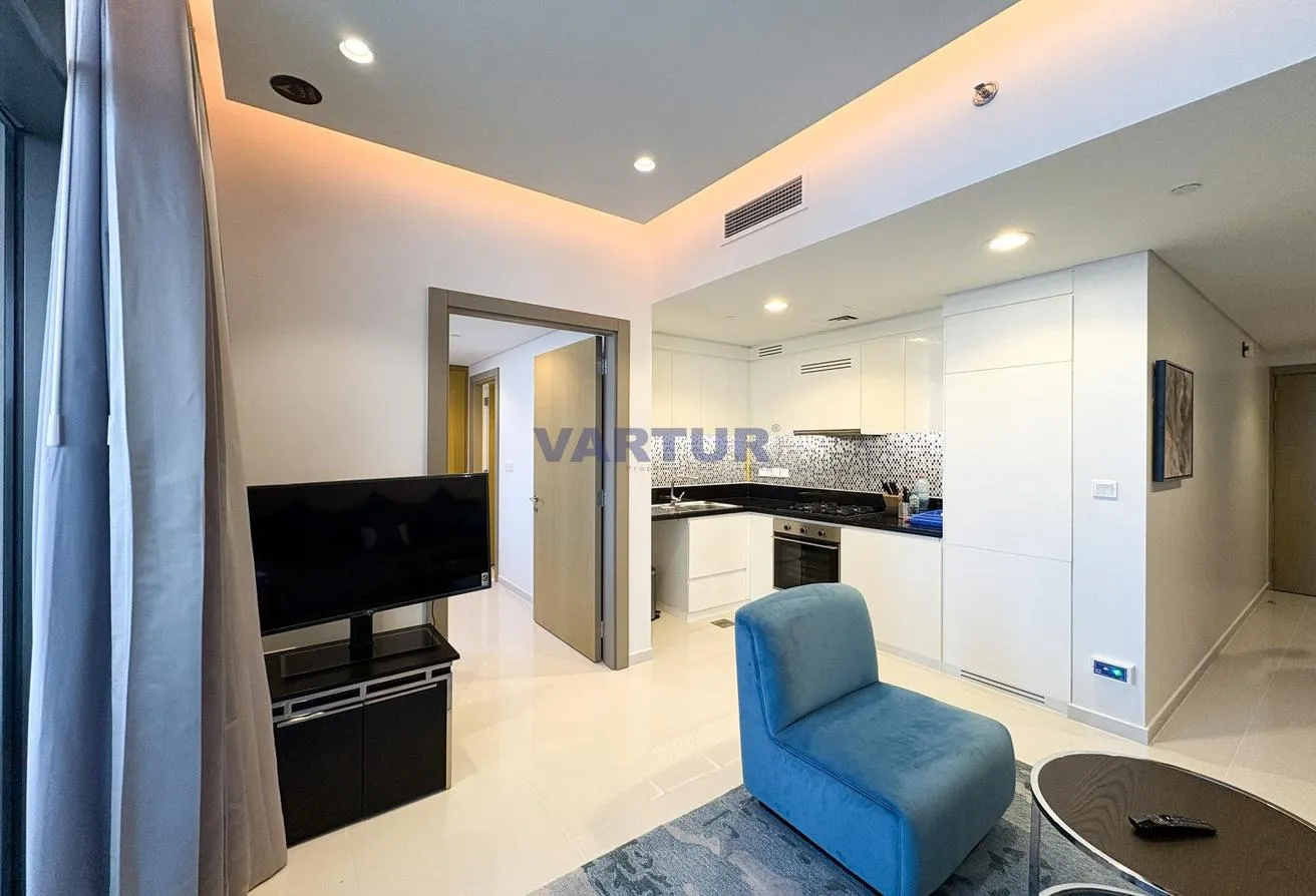 Photo of the living area opening onto the white kitchen, with a TV unit and an armchair