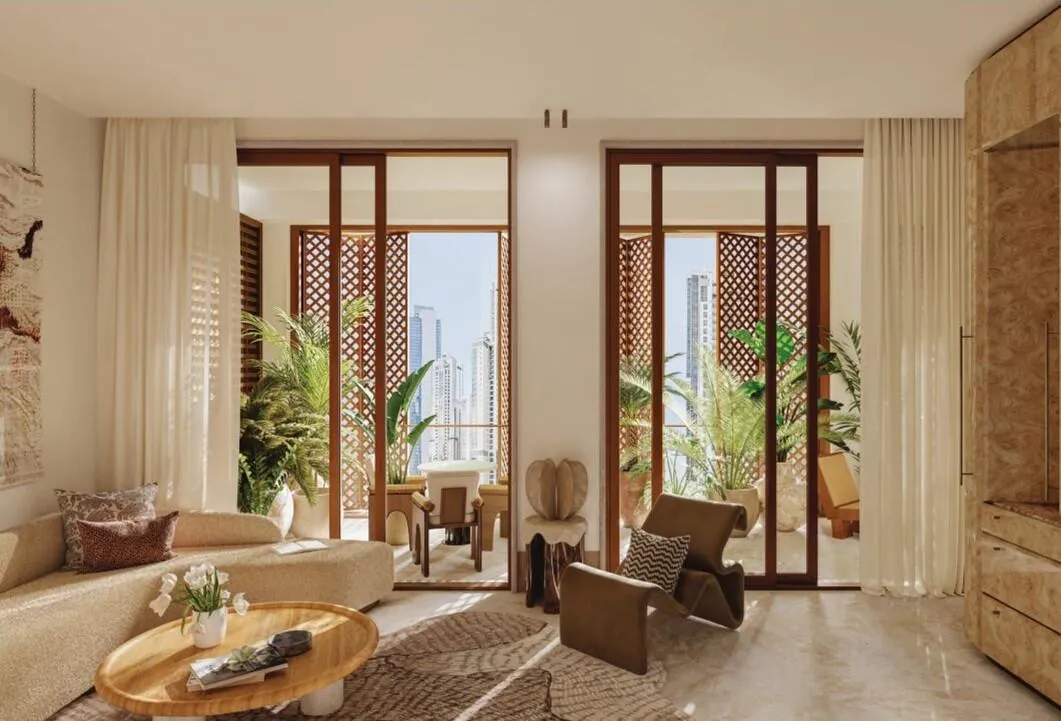 A living room with a pale sofa and armchair, a round table between them and glazed doors to the balcony