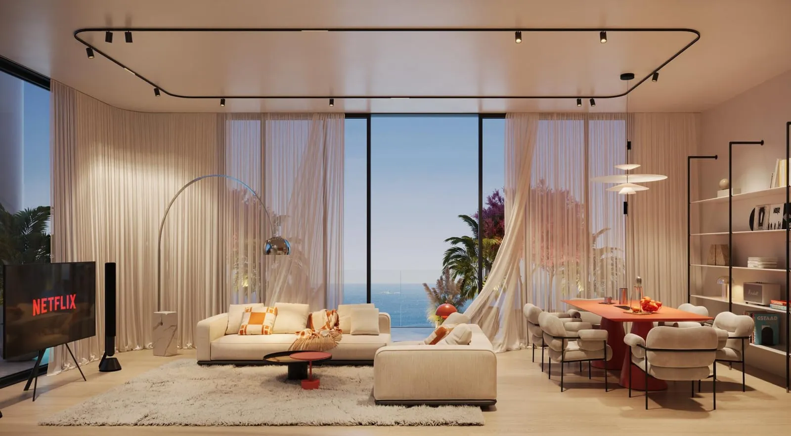 A living room with a wall-mounted television and a corner sofa, full-height glazing opening to the sea