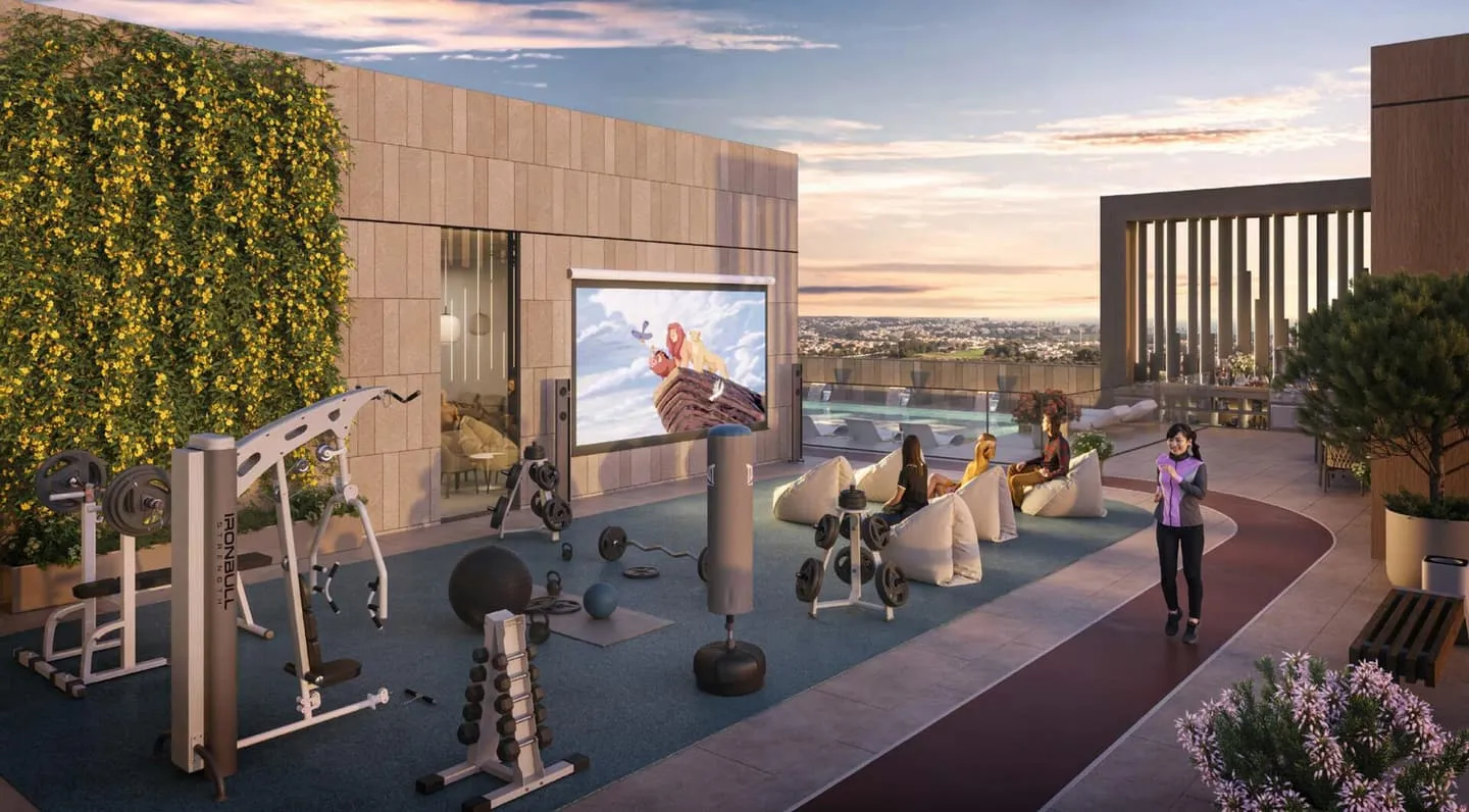 An outdoor cinema screen with bean bags beside open-air gym equipment and a jogging track along a green wall