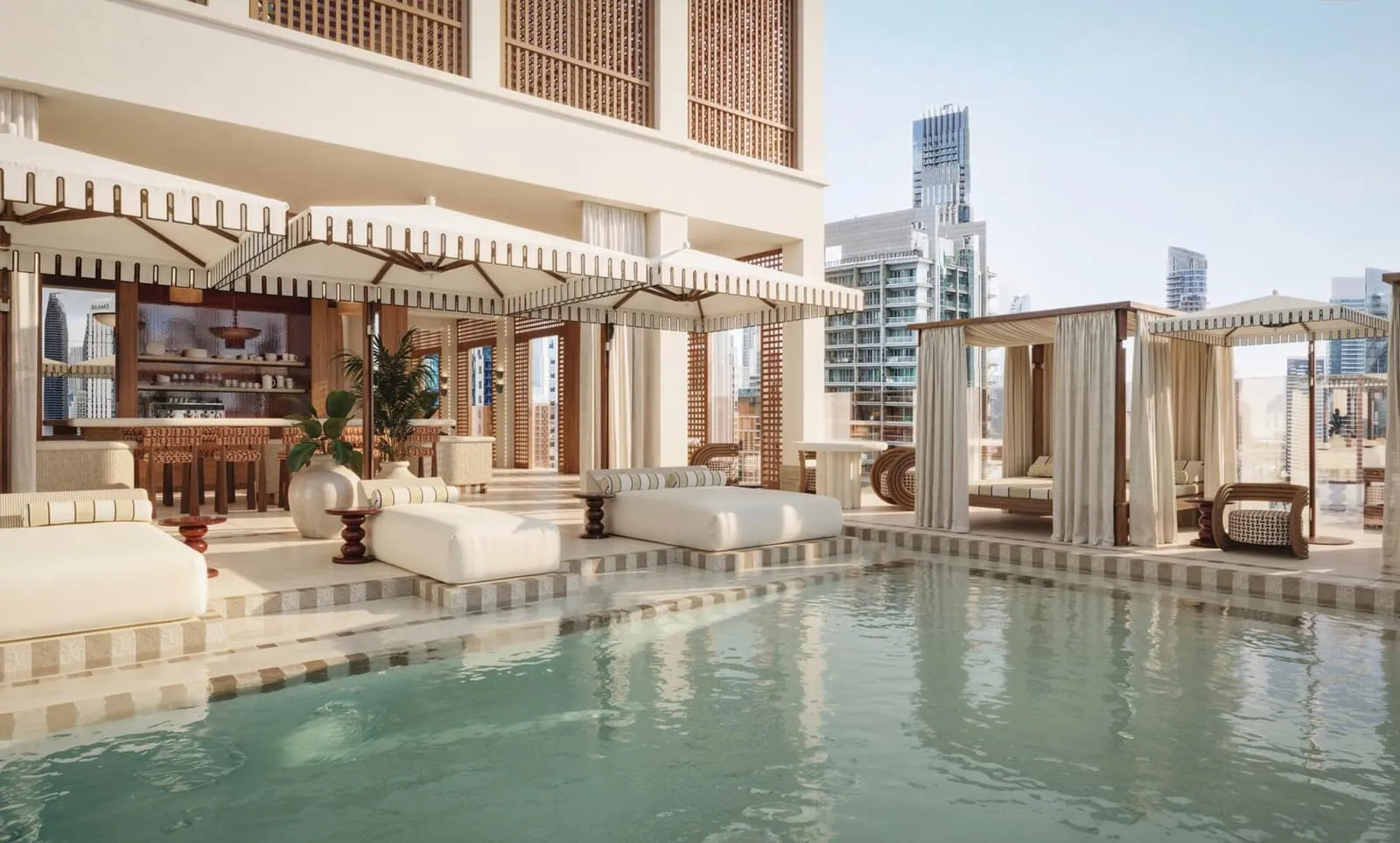 The pool deck by day, sun beds along the water and a covered lounge under the building