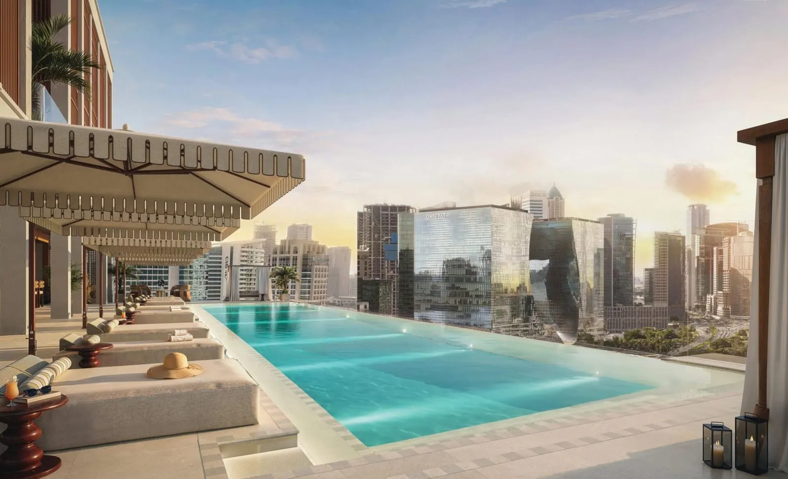 A pool at sunset, sun loungers along one edge and the city towers on the horizon beyond the deck