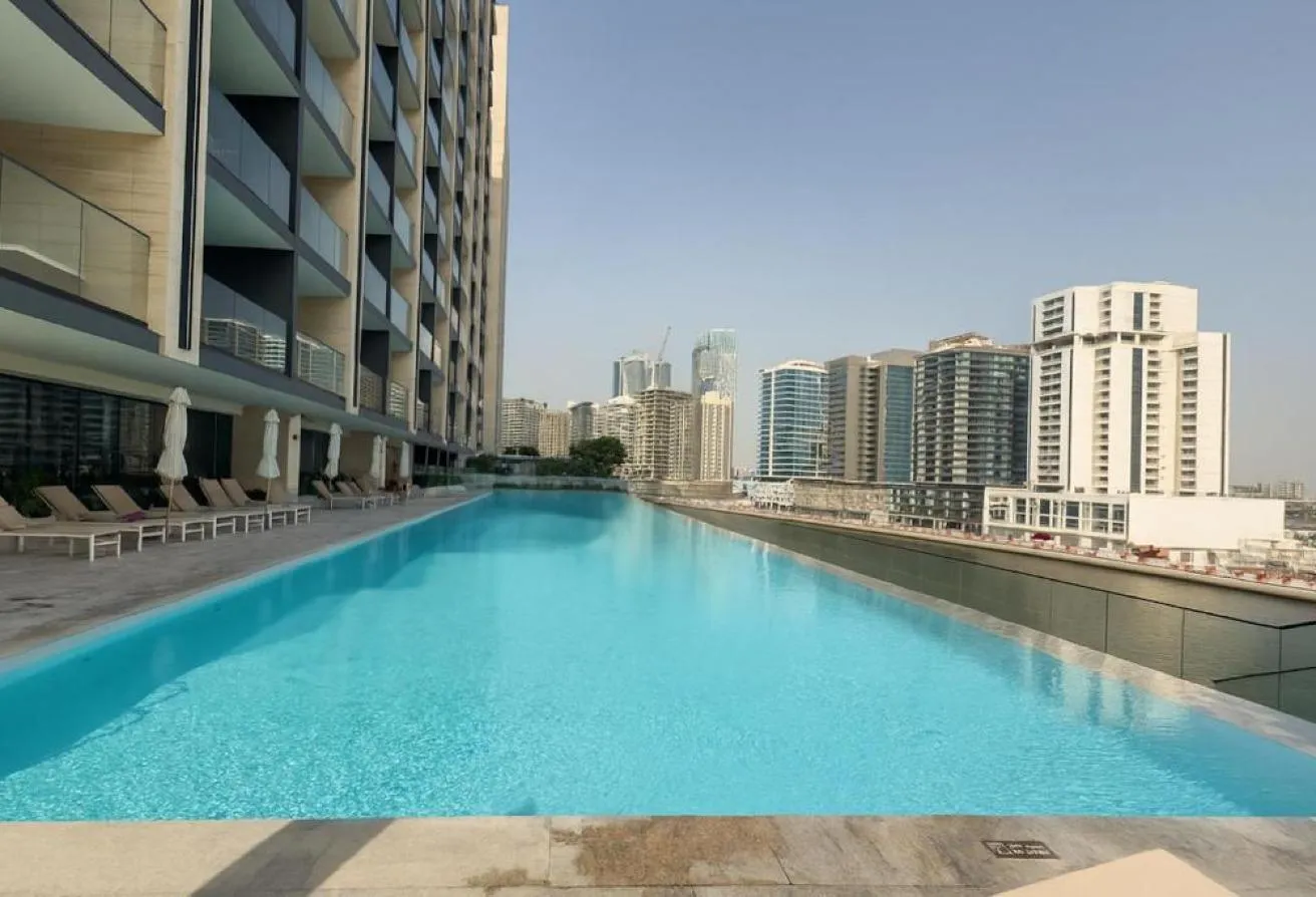 Photo of the pool deck along the tower's side, with loungers by the water and neighbouring towers beyond