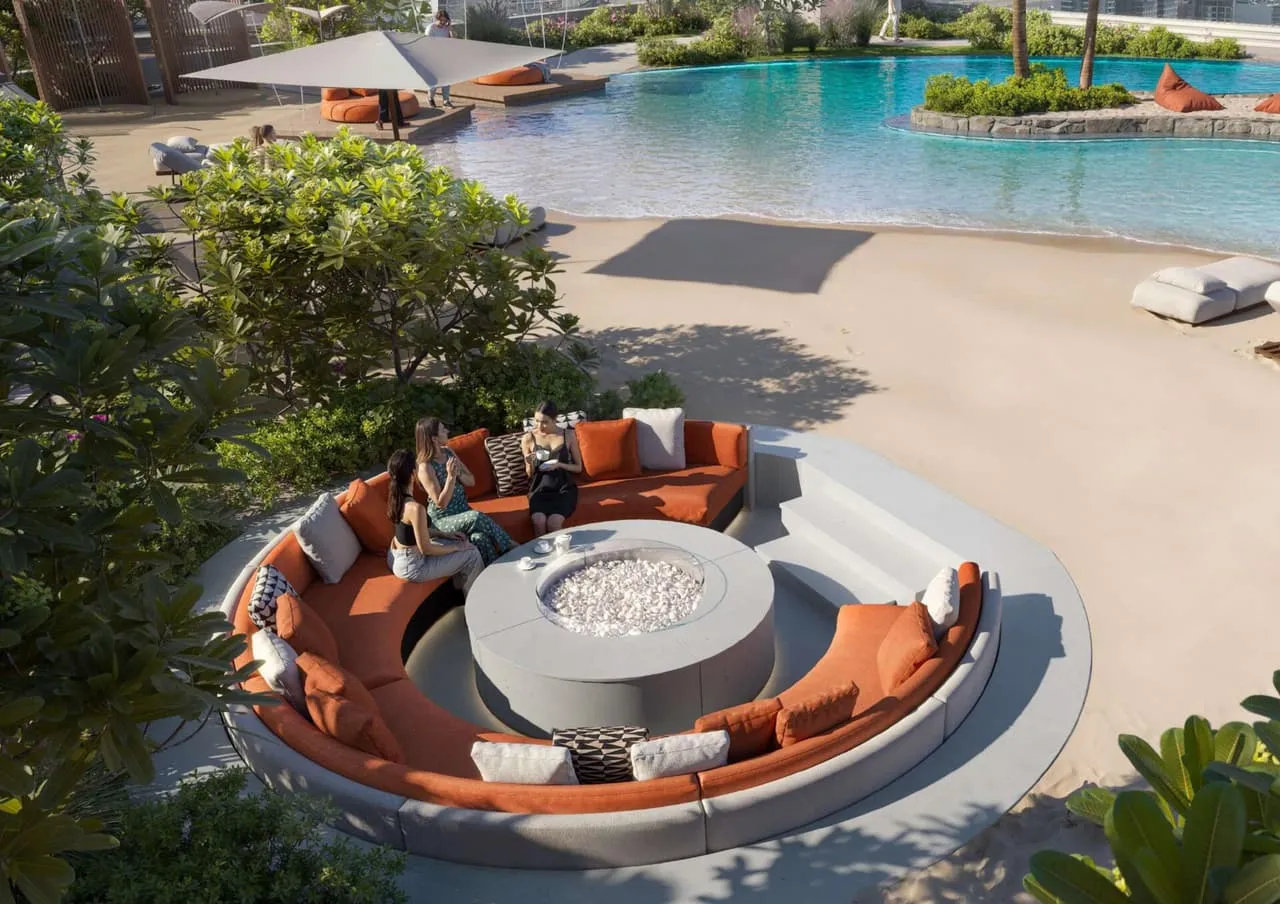 A circular seating pit beside the pool, sand underfoot and planting around it