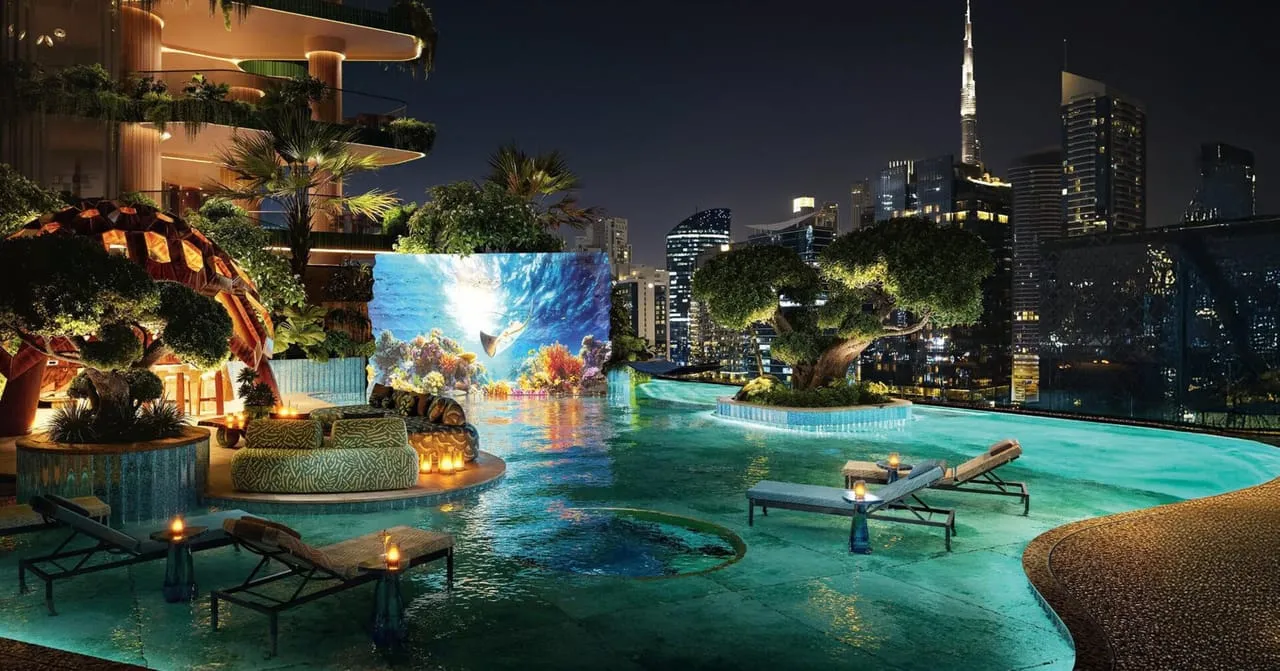The pool terrace at night, the water lit from below and the skyline standing behind the planting