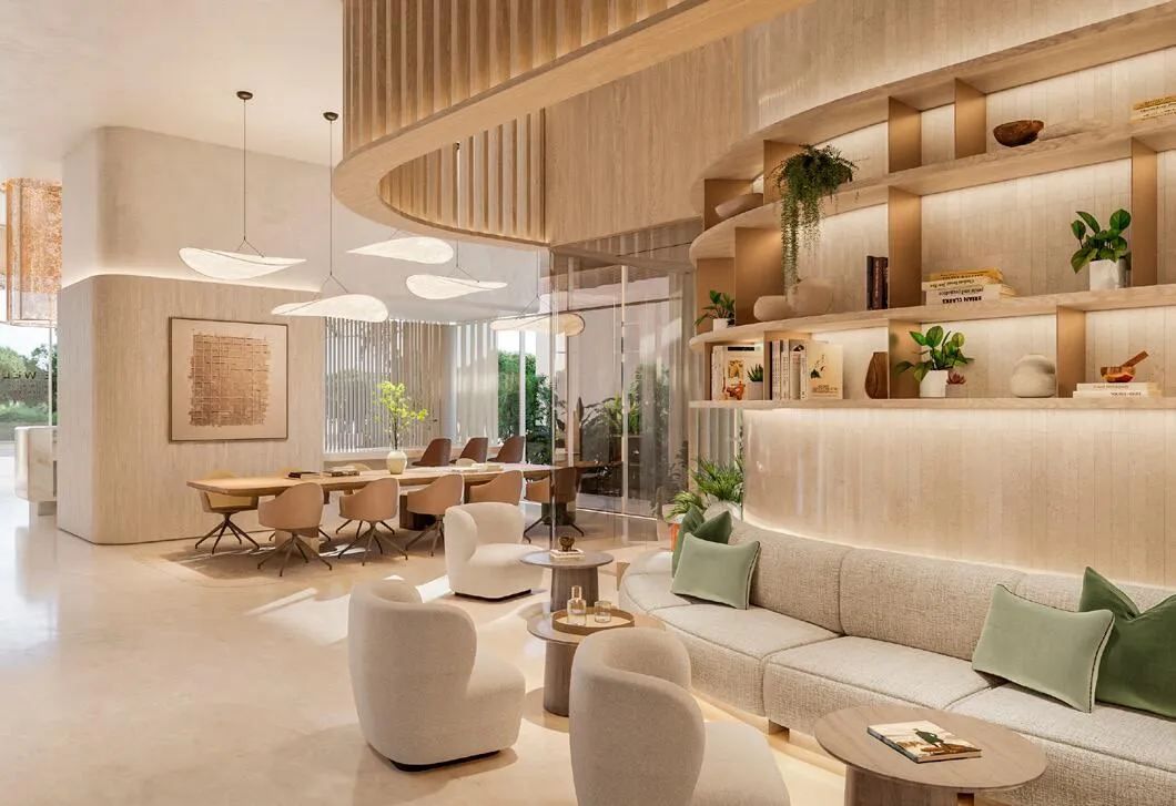 A residents' lounge with sofas, a long table and curved shelving filled with books and plants