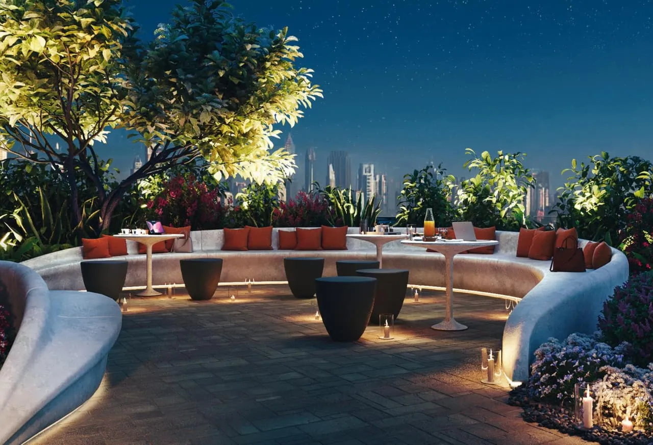 A rooftop garden at dusk, a long curved bench and firepits set among trees above the city