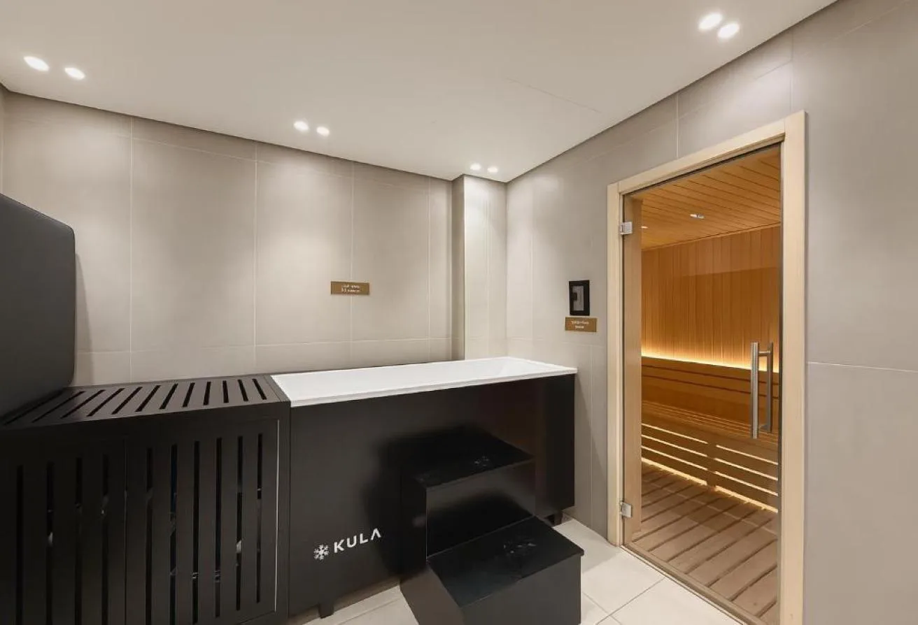 Photo of a sauna behind a glass door, with a black tub and steps in front