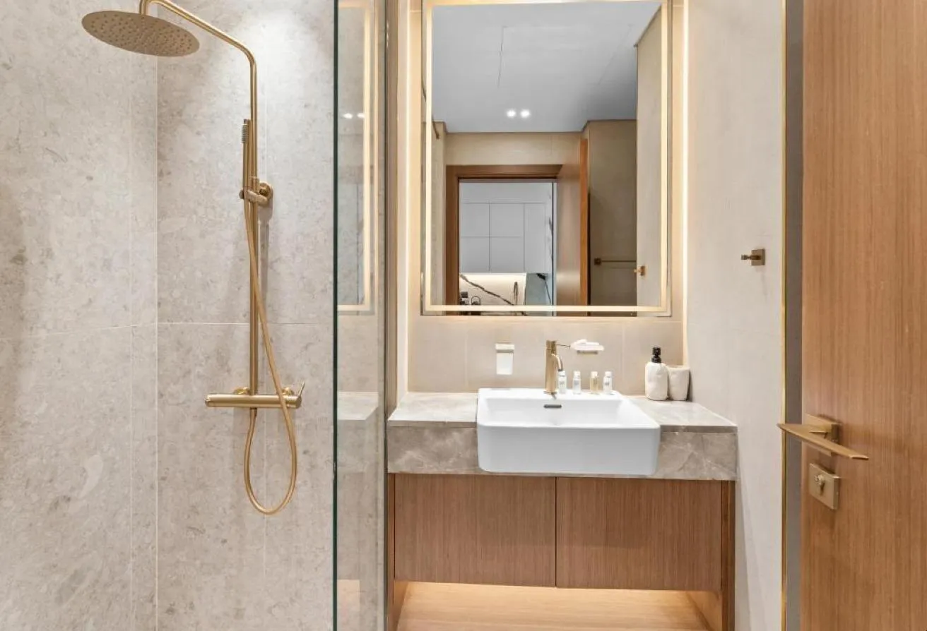 Photo of the shower with gold-toned fittings, beside a vanity and mirror