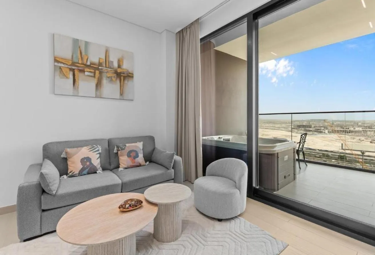 Photo of a grey sofa and round tables by the glass door, with the hot tub on the balcony
