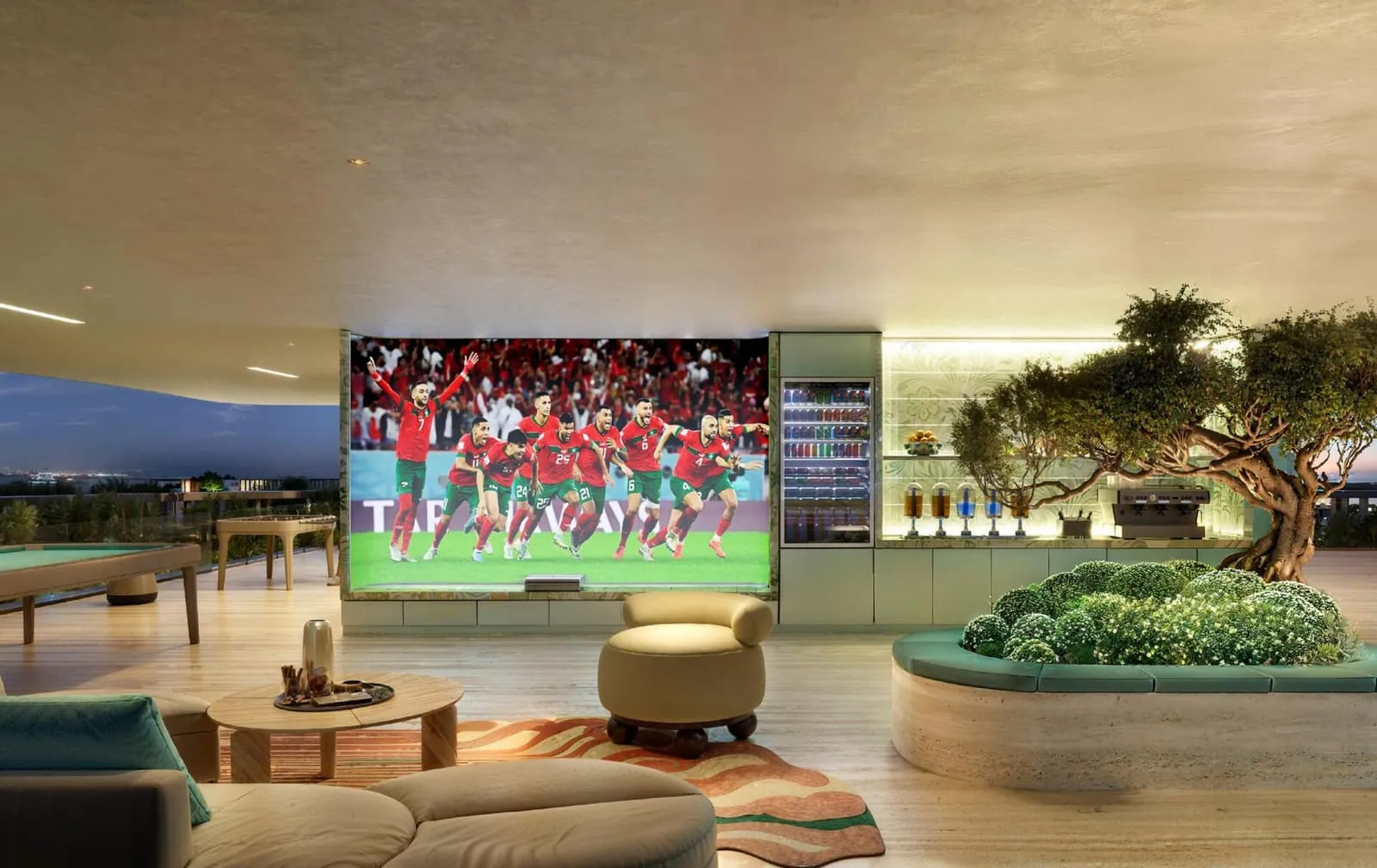 A sports lounge with a large screen, a pool table and an olive tree planted in the floor