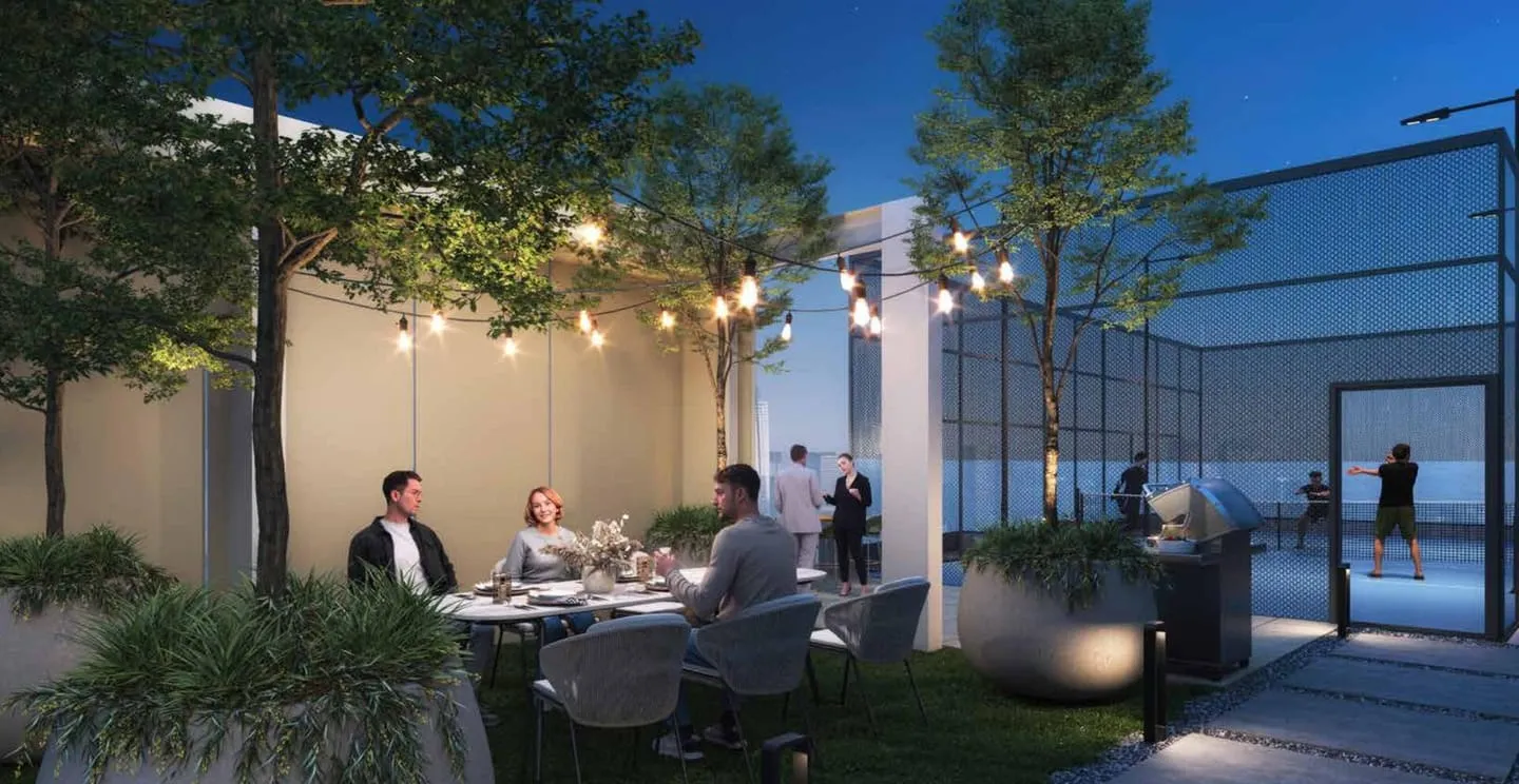 The podium terrace at dusk, residents dining under festoon lights beside a barbecue station and a fenced sports court