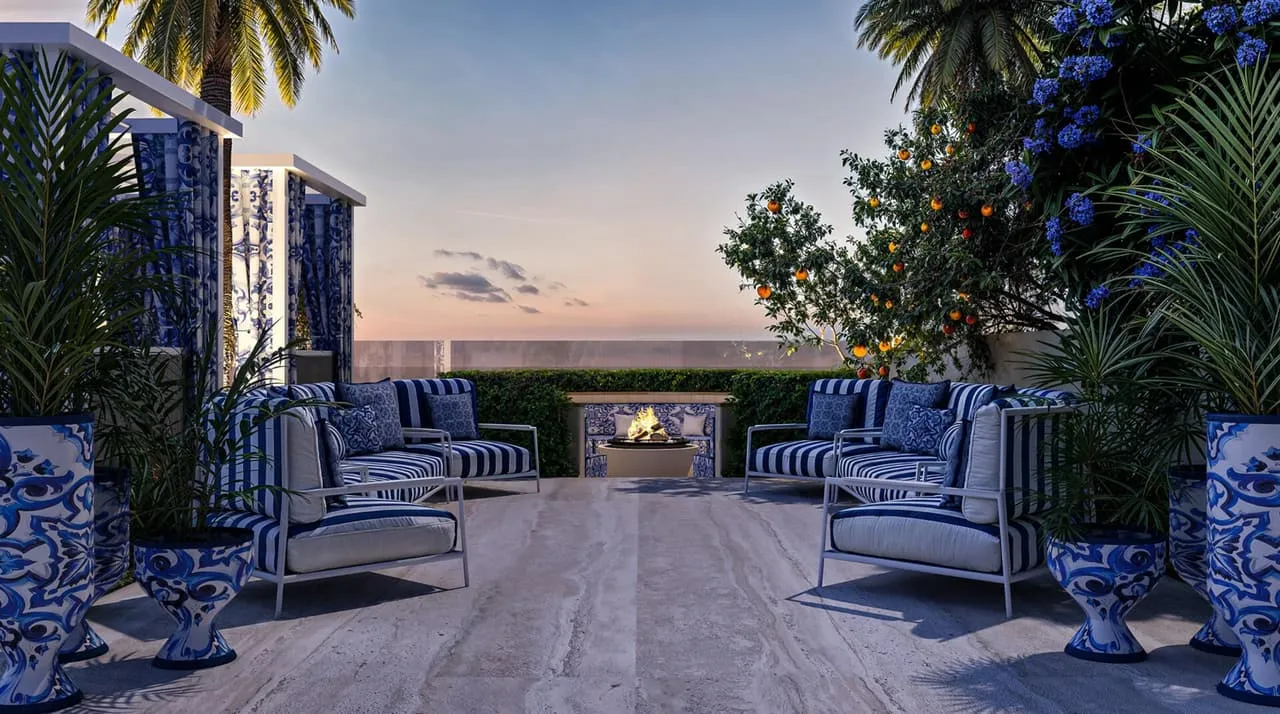 An outdoor lounge in blue and white patterned upholstery, tall glazed planters and palms framing the sunset