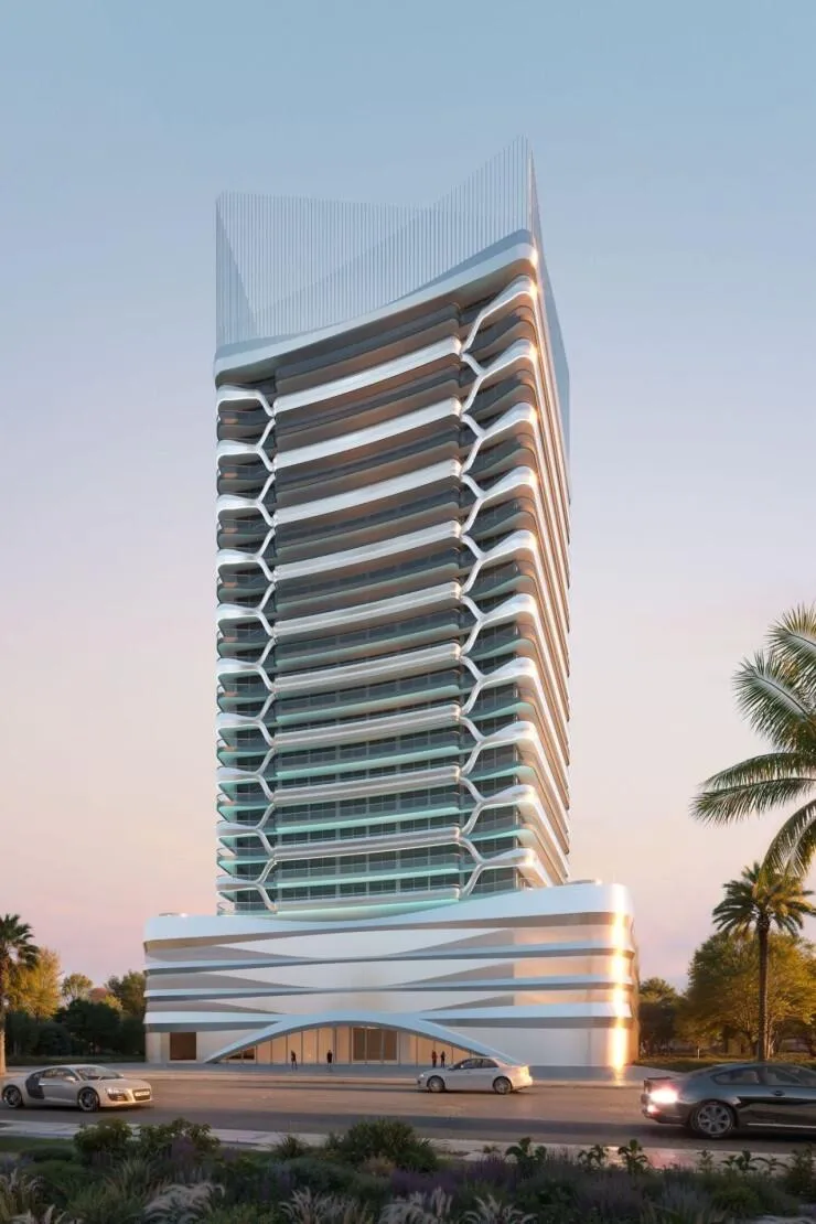 The tower in daylight against a clear sky, white balcony bands stacked above a curved podium, palms and parked cars at the kerb