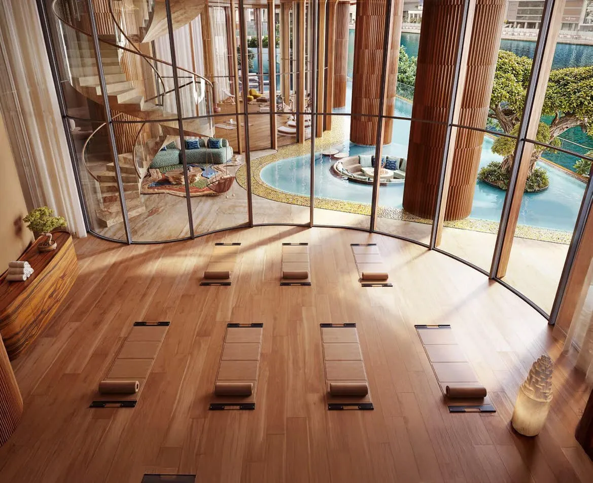 A studio with mats laid out in rows on a timber floor, the pool visible through the curved glazing
